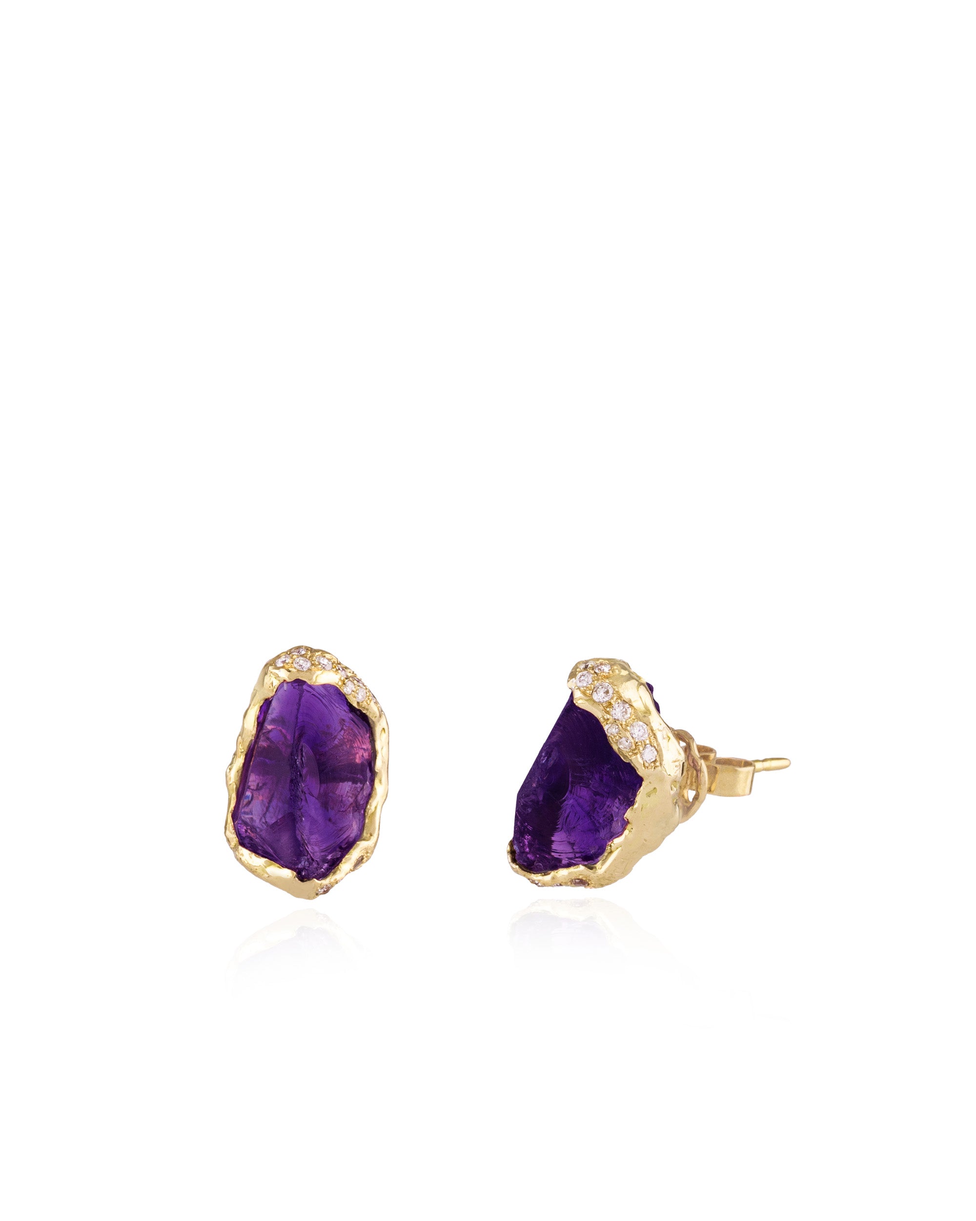 Pair of stud earrings made with raw, deep purple amethyst stones set in textured 18K yellow gold bezels, trimmed with pavé-set diamonds along the upper edges.
