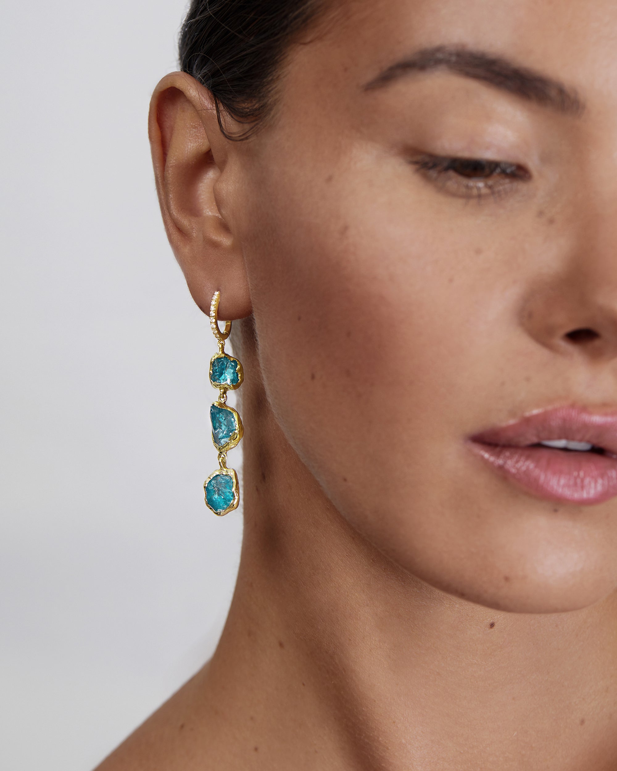 Model wearing Natalie Dissel 14K yellow gold drop earring featuring three raw Blue Apatite gemstones hanging from a diamond hoop, Rough Rocks collection.