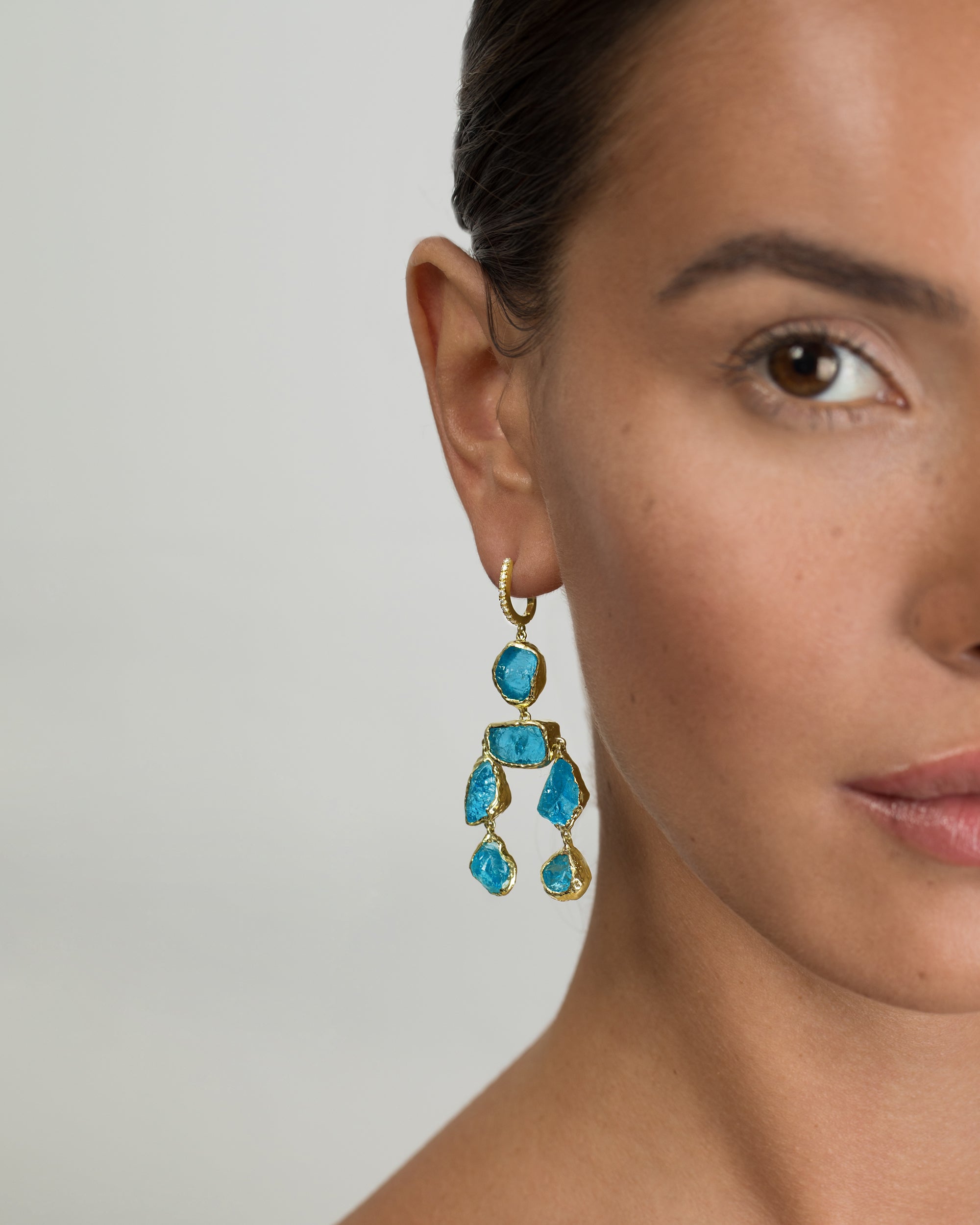 Close-up model shot of a woman wearing a recycled 14K Yellow Gold chandelier earring made with raw blue apatite stones and a diamond-paved hook ear wire. 