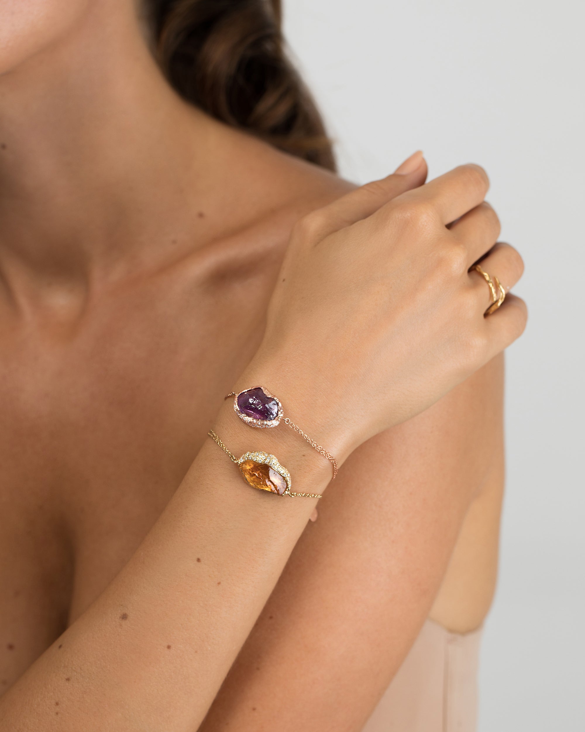 Model wearing stacked Natalie Dissel fine chain bracelets featuring raw amethyst and golden citrine stones set in diamond-paved gold caps