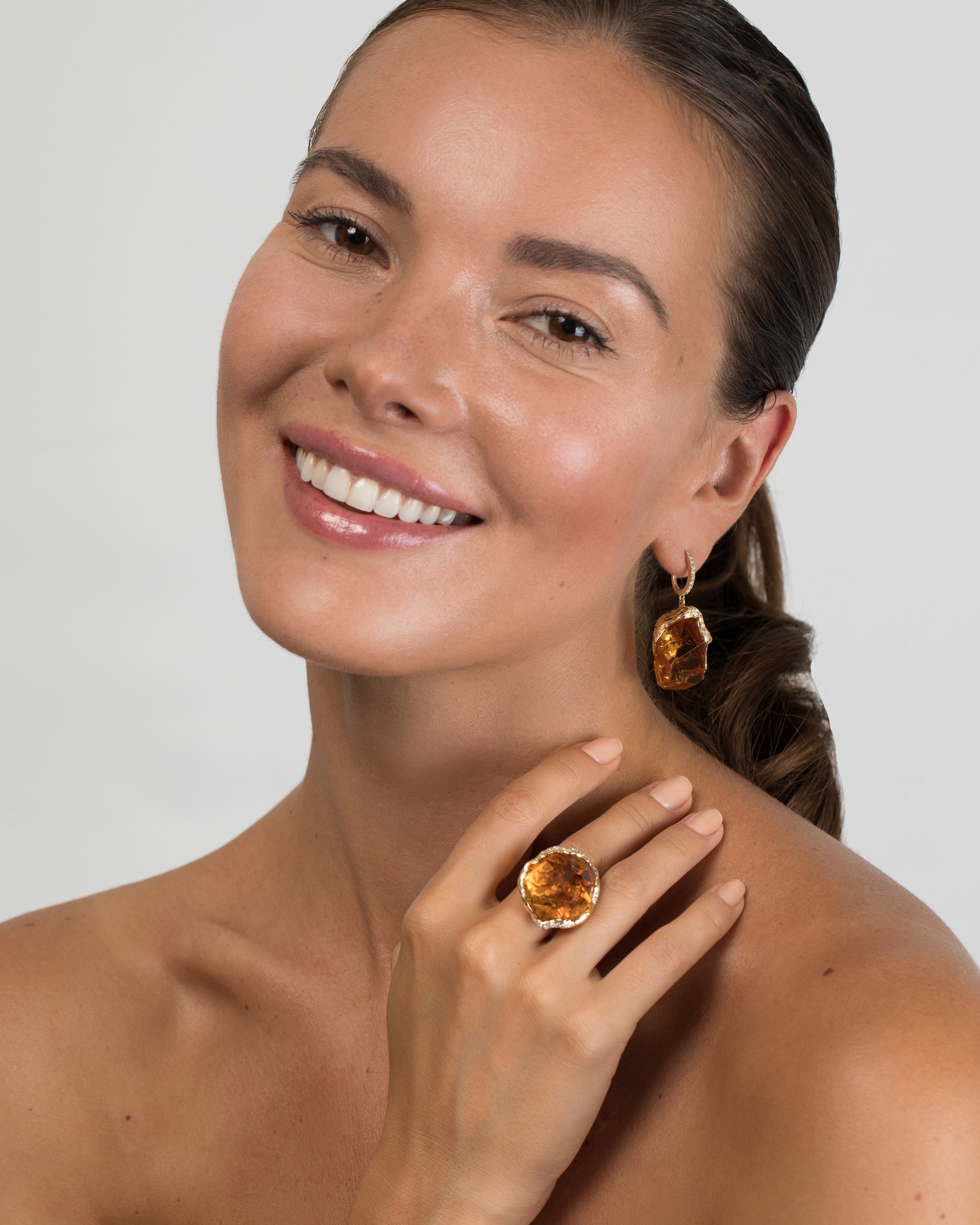 Close-up of a model, showcasing a statement 18K yellow gold ring with a large, freeform citrine stone and diamond accents, along with matching citrine drop earrings.