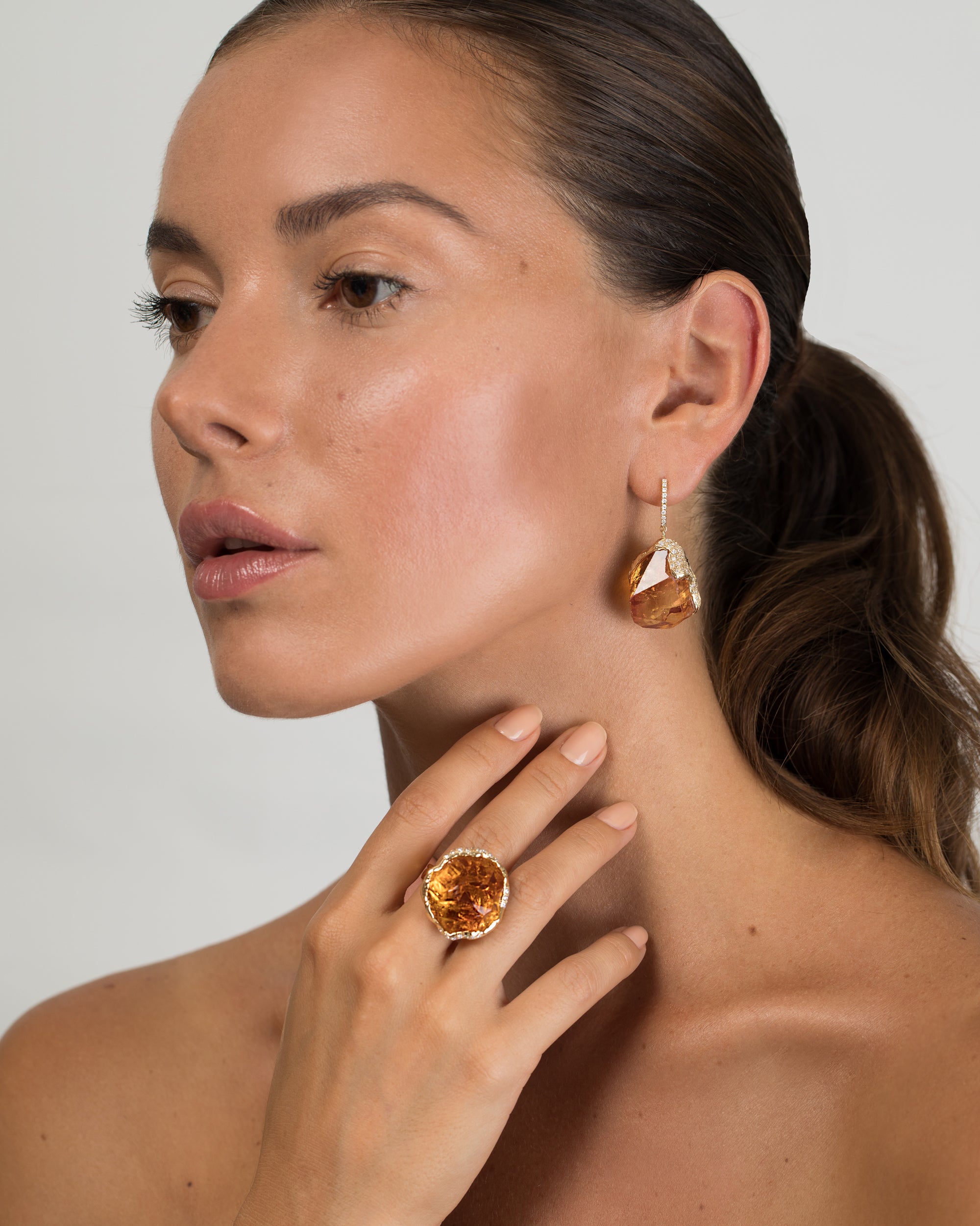 Model wearing a large, raw-cut citrine ring set in 18K gold and matching statement drop earrings.