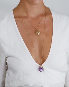 Close-up view of model showcasing layered Natalie Dissel 18K yellow gold gemstone pendant necklaces against a white v-neck top.