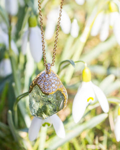 Close-up of Natalie Dissel 18K yellow gold pendant featuring a raw Prasiolite gemstone with a pavé diamond cap, set against white snowdrop flowers.