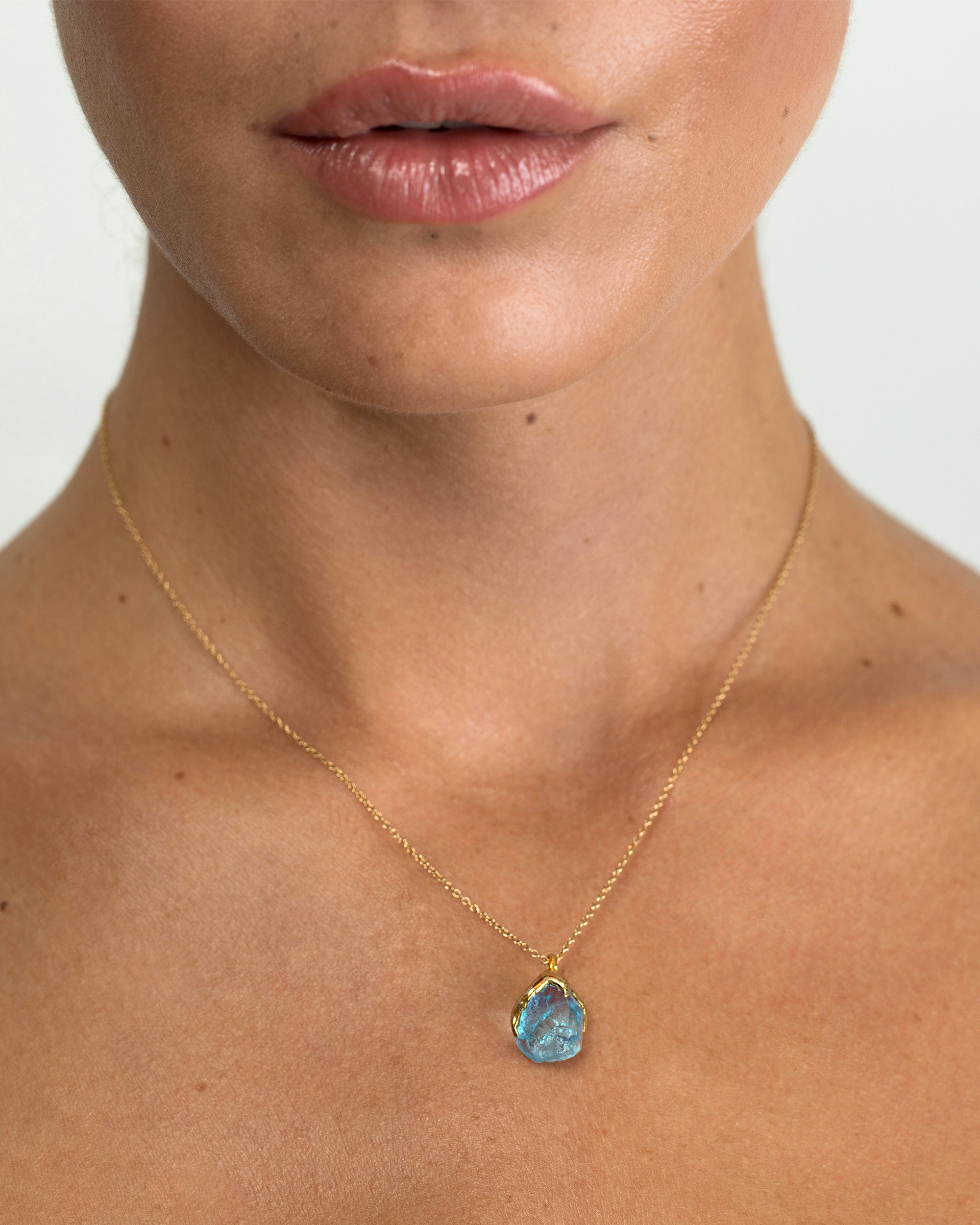 Close-up of model wearing Natalie Dissel 18K yellow gold necklace with a raw Sky Blue Topaz gemstone pendant, Rough Rocks collection.
